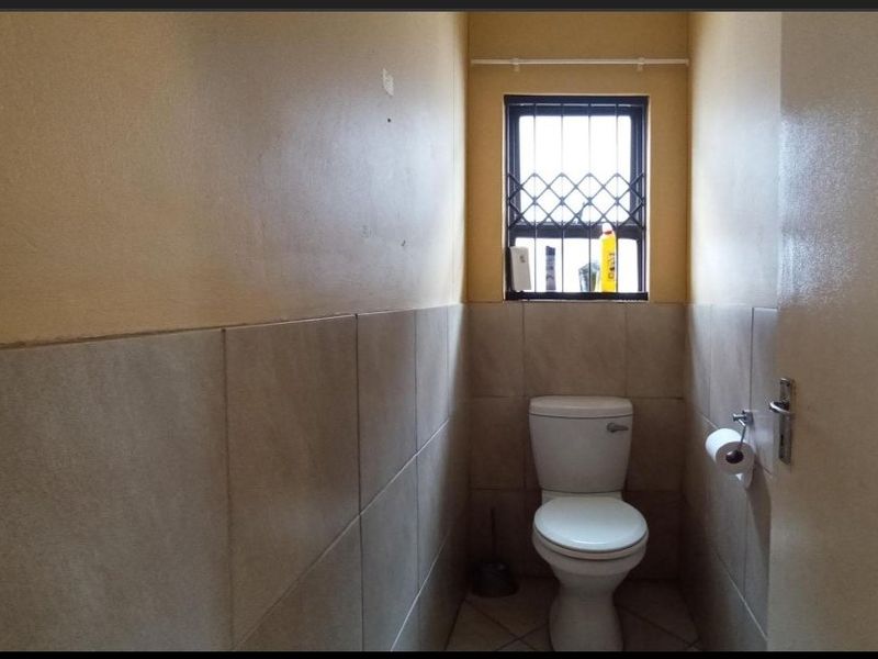 A compact guest bathroom featuring tiled walls, a standard toilet, and a window with a security gate.