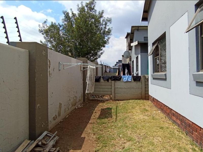 Rear exterior view of the townhouse featuring a small lawn area, perimeter wall with electric fencing, and brick-based exterior wall finish.