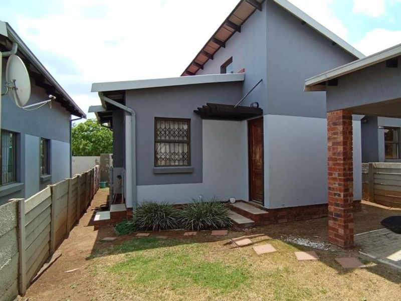 Rear exterior view of the townhouse featuring a small garden area, brick pillar, and security features on the windows and doors.