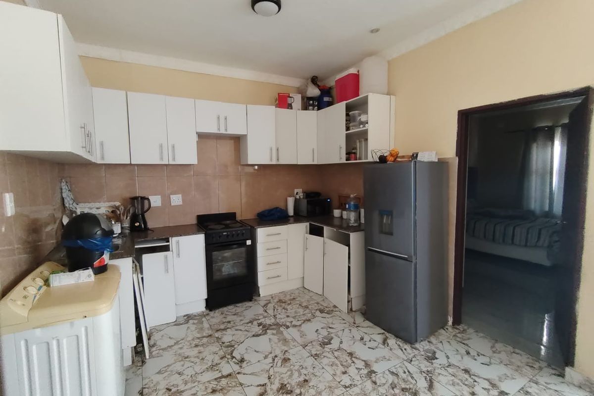 A functional kitchen featuring white cabinetry, tiled backsplash, and patterned floor tiles, requiring some maintenance and cosmetic updates.