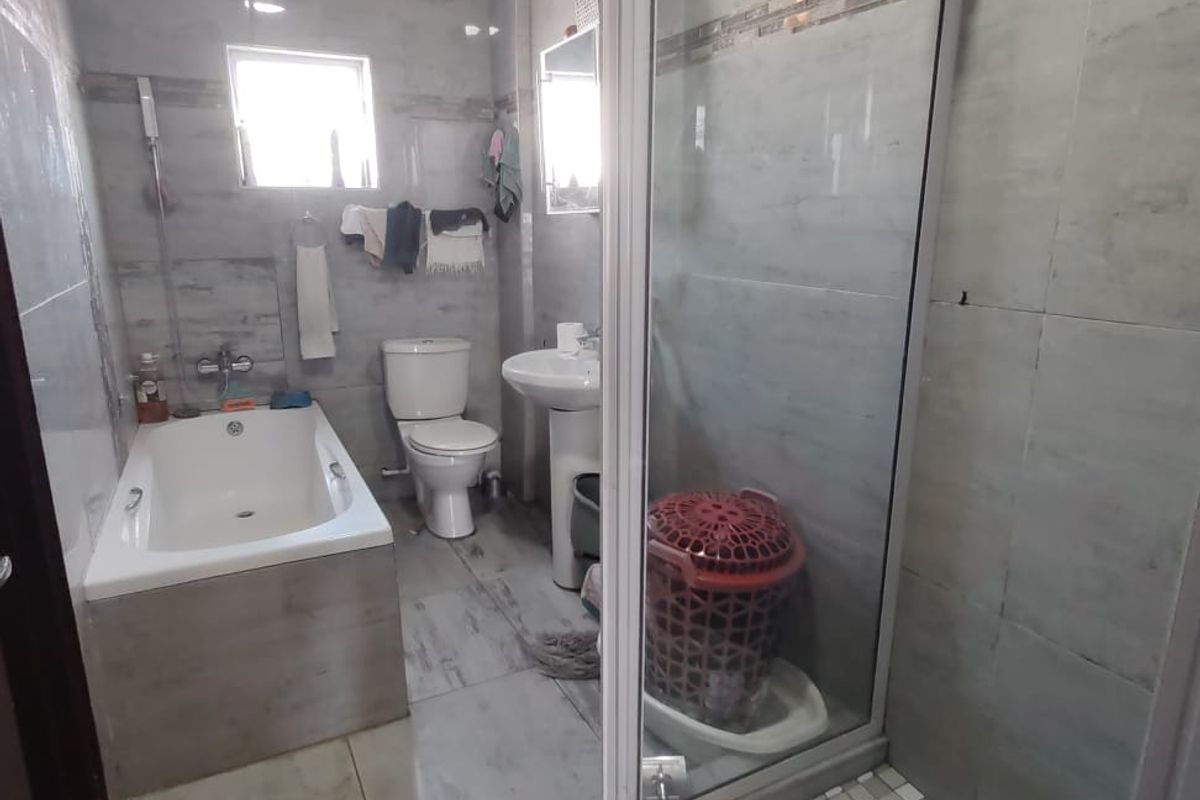 A modern bathroom featuring a built-in bathtub, a separate glass-enclosed shower, a pedestal sink, and neutral grey wall and floor tiling.