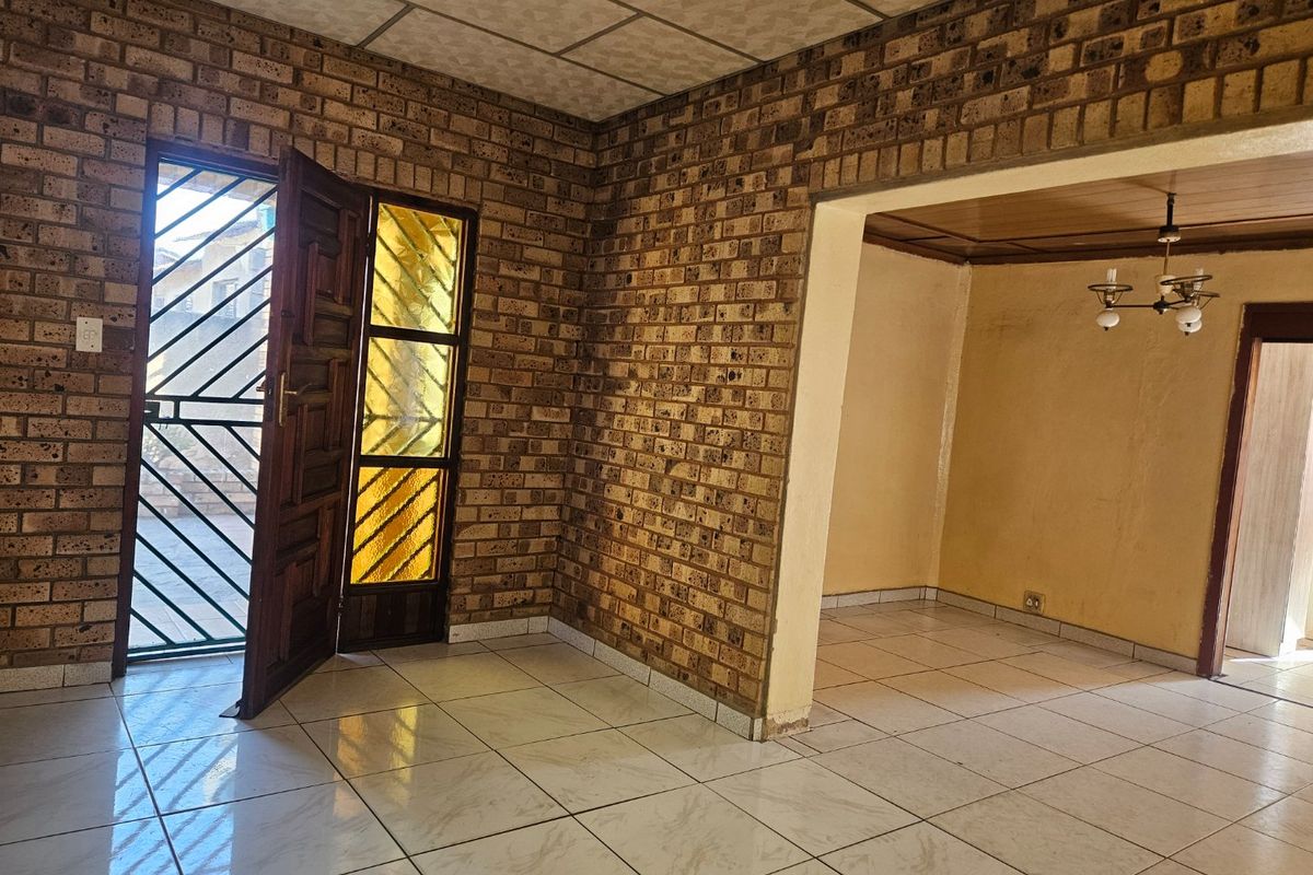 An empty living area featuring exposed brick walls, ceramic tiled flooring, and a combination of drop ceiling and timber paneling finishes.
