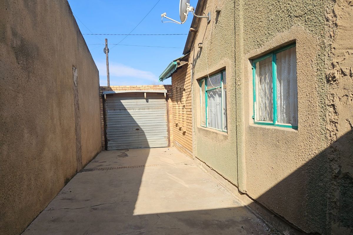 Rear exterior view showing a concrete driveway, a metal roller garage door, and the side elevation of the house with security-fitted windows.