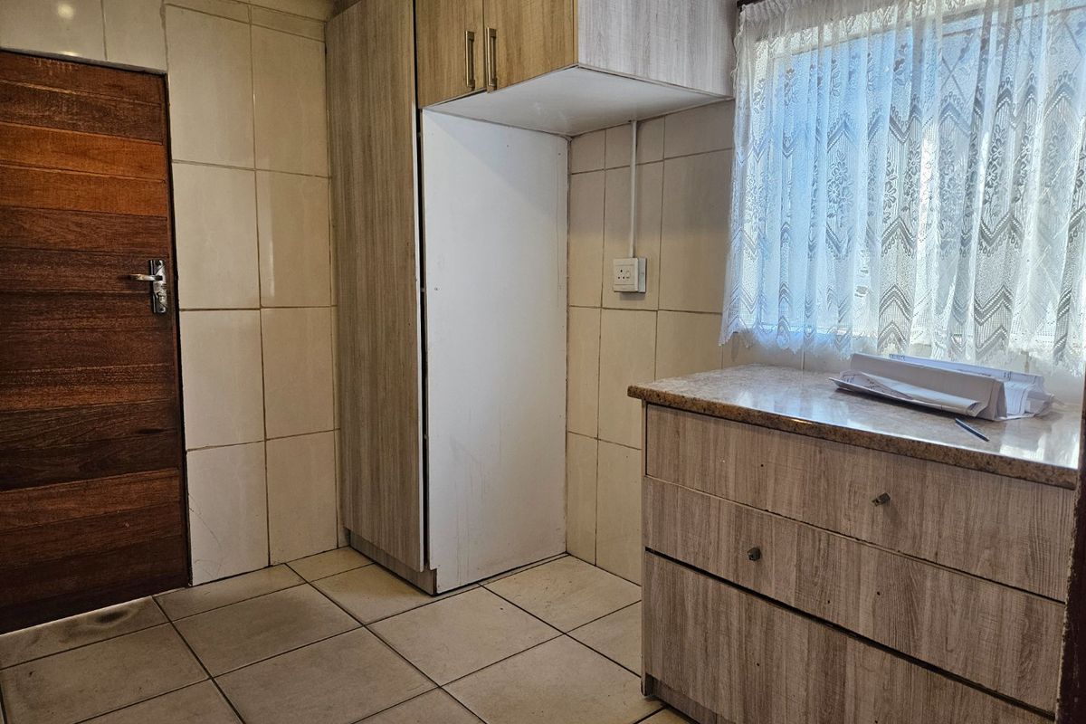 A functional kitchen area featuring tiled walls and flooring, built-in cabinetry with stone countertops, and a timber door.