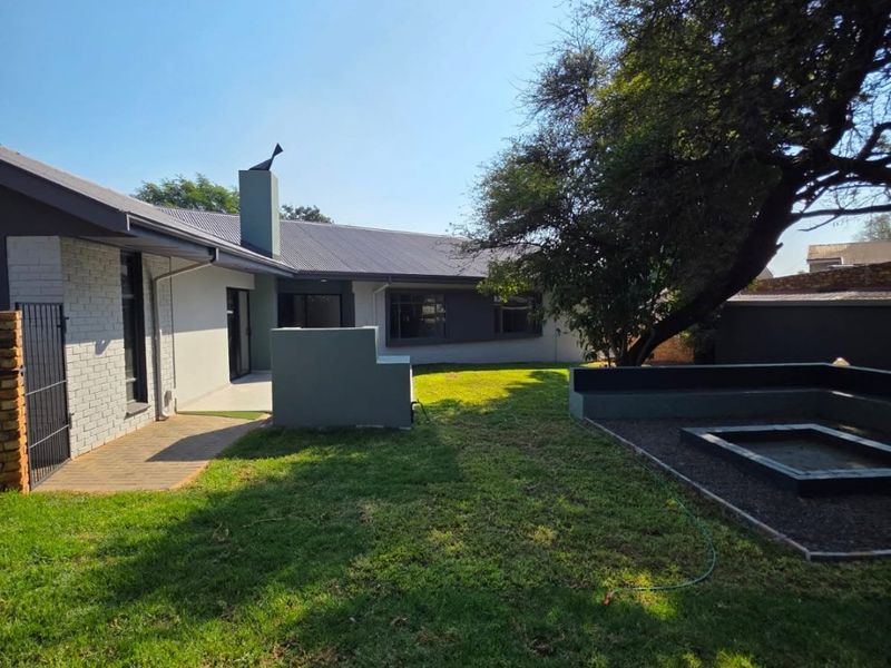 A well-maintained rear garden featuring a paved patio area, a built-in fire pit with surrounding seating, and a modern exterior facade.