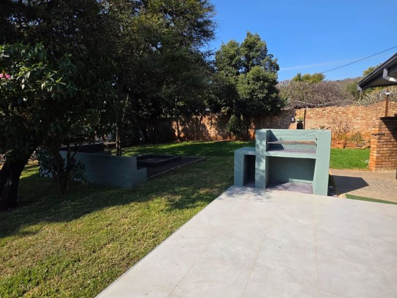 A spacious outdoor patio featuring a built-in braai, overlooking a well-maintained garden with a brick boundary wall.