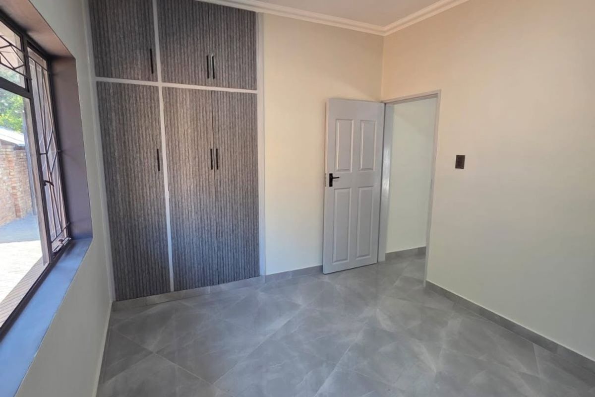 A clean, empty bedroom featuring modern grey tiled flooring, built-in cupboards with textured finish, and a neutral color palette.