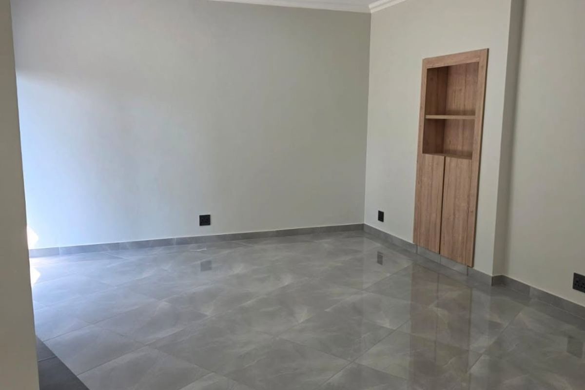 A bright, modern living area featuring polished porcelain floor tiles, recessed downlighting, and a built-in wooden shelving unit.