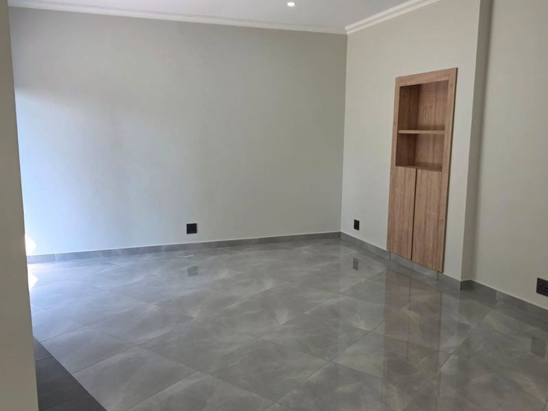 A bright, modern living area featuring polished porcelain floor tiles, recessed downlighting, and a built-in wooden shelving unit.