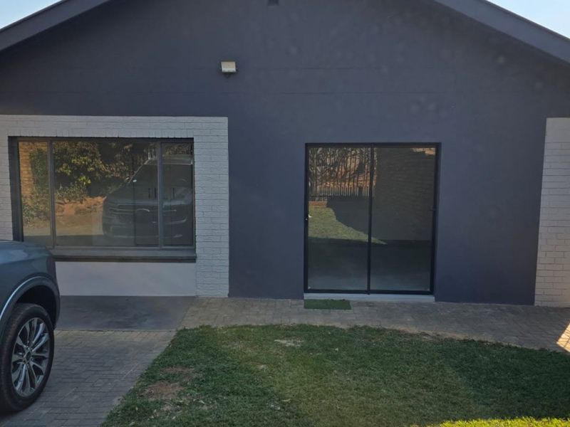 Rear exterior view of the house featuring a paved walkway, lawn, sliding glass door, and large window with dark grey painted facade.