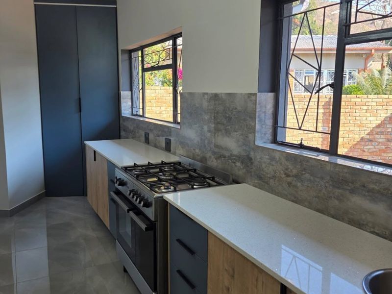Modern kitchen featuring two-tone cabinetry, stone countertops, a gas stove with oven, and tiled flooring with natural light from large windows.