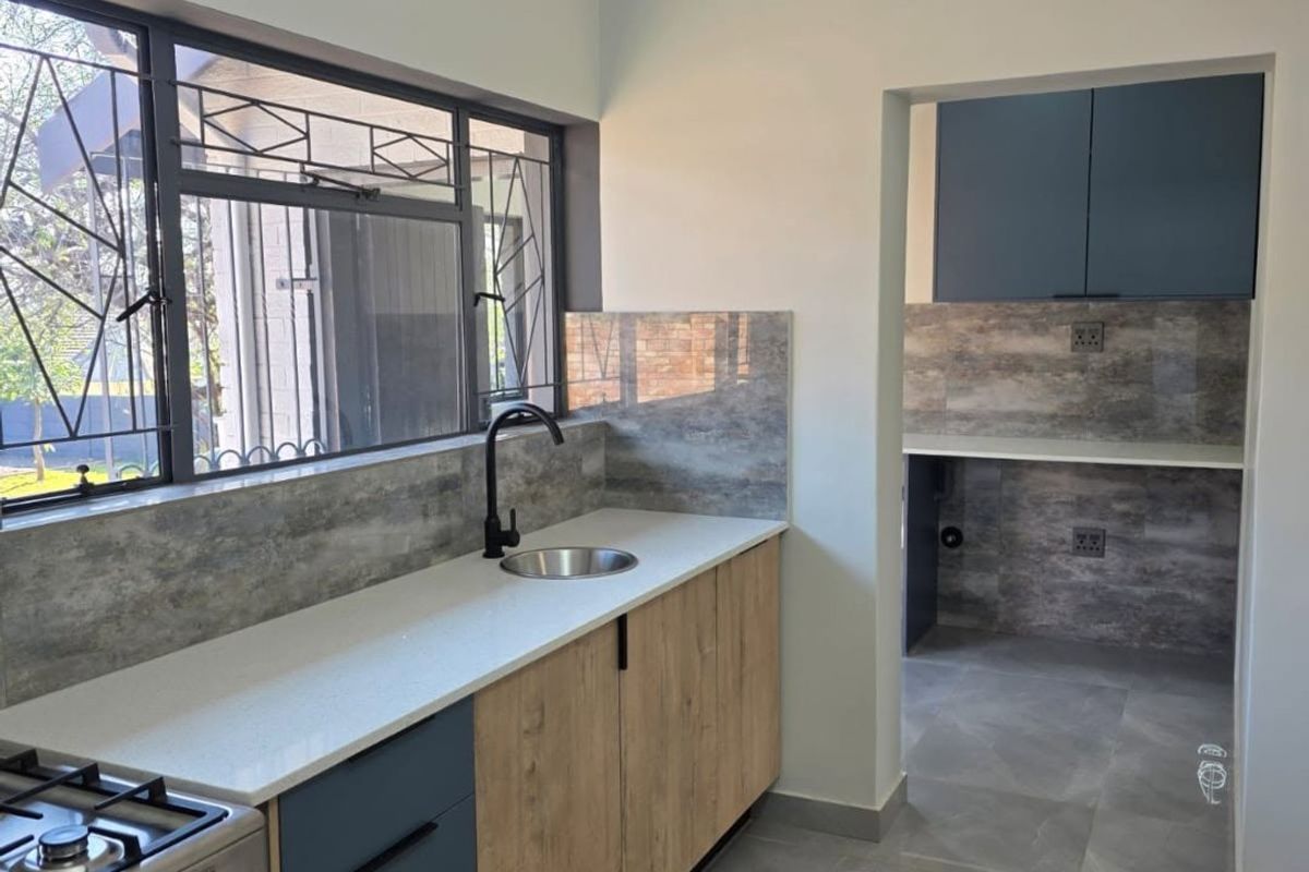 Modern kitchen featuring stone countertops, two-tone cabinetry, gas stove, and a separate scullery area with matching finishes and tiled flooring.