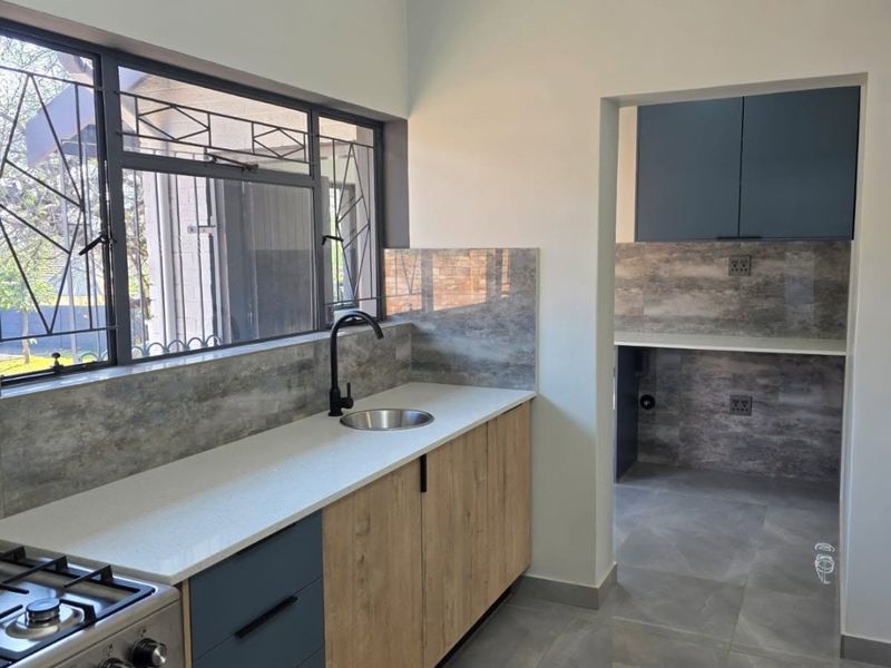 Modern kitchen featuring stone countertops, two-tone cabinetry, gas stove, and a separate scullery area with matching finishes and tiled flooring.