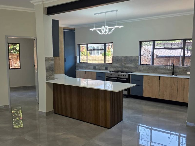 Modern, renovated kitchen featuring a central island, stone countertops, built-in gas hob, and sleek cabinetry with high-quality porcelain floor tiles.