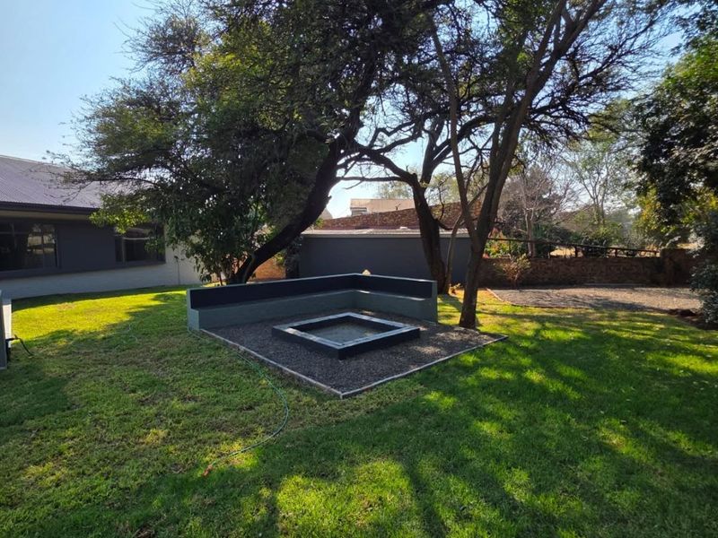 A well-maintained garden area featuring a built-in fire pit with integrated bench seating, surrounded by mature trees and a manicured lawn.