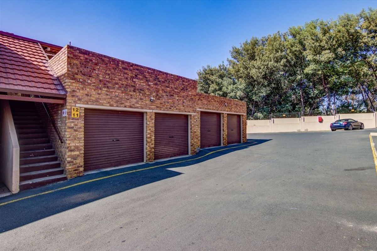A row of four brick-faced garages with roller doors, featuring an adjacent external staircase and paved driveway area.