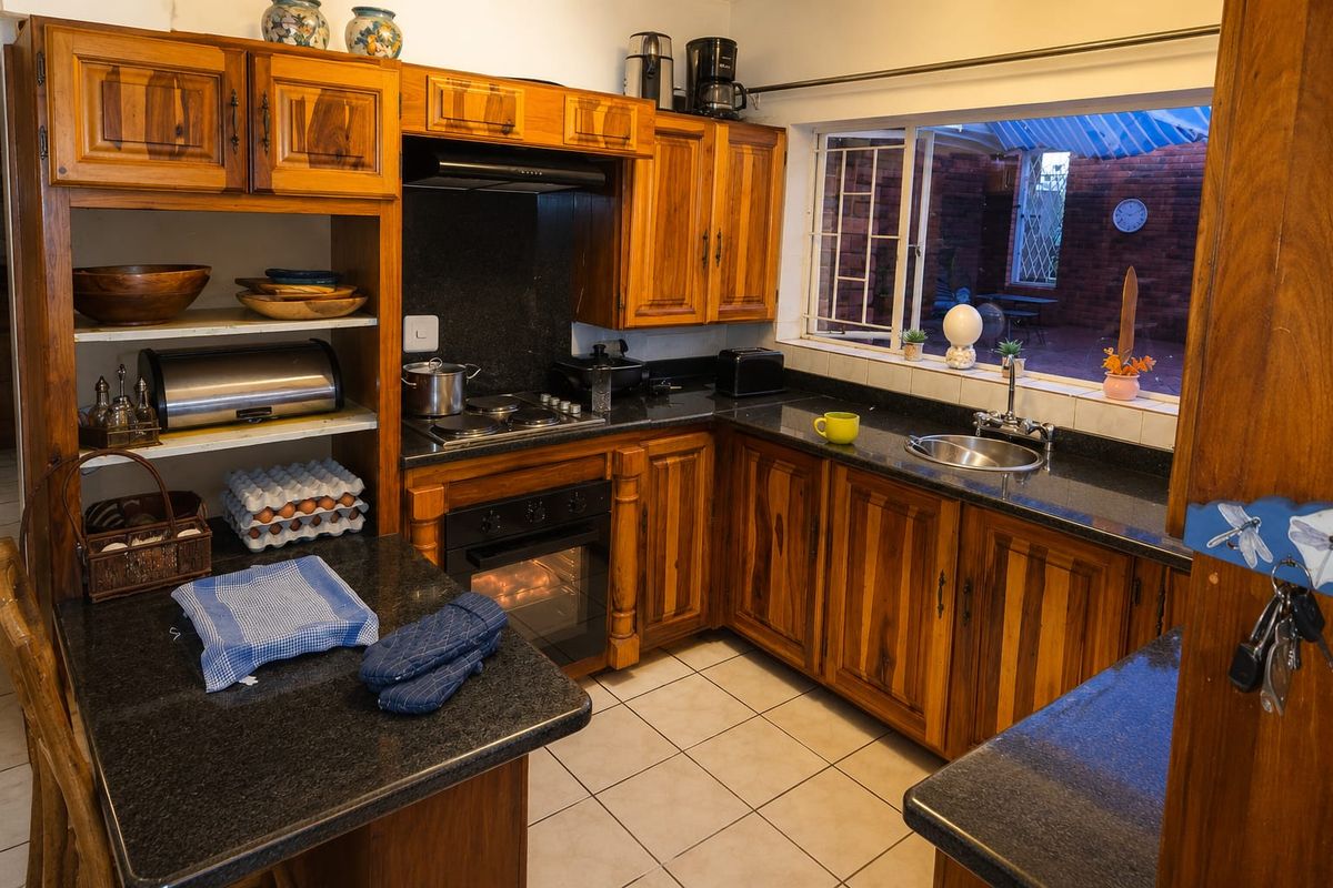 A functional kitchen featuring warm wooden cabinetry, dark granite countertops, built-in oven, electric hob, and a window overlooking the rear patio area.