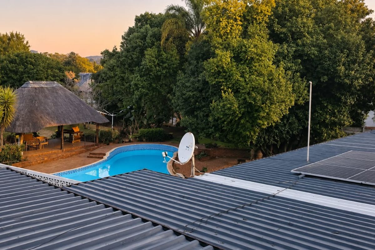 Aerial view of the property featuring a corrugated metal roof with solar panels, a swimming pool, and a thatched lapa in the garden.