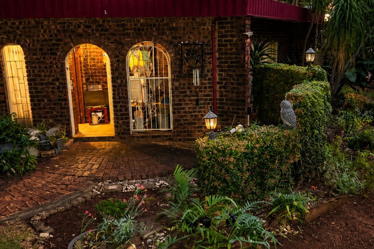 A rear exterior view of a brick house featuring arched doorways, security gates, and a paved patio area leading into a landscaped garden.