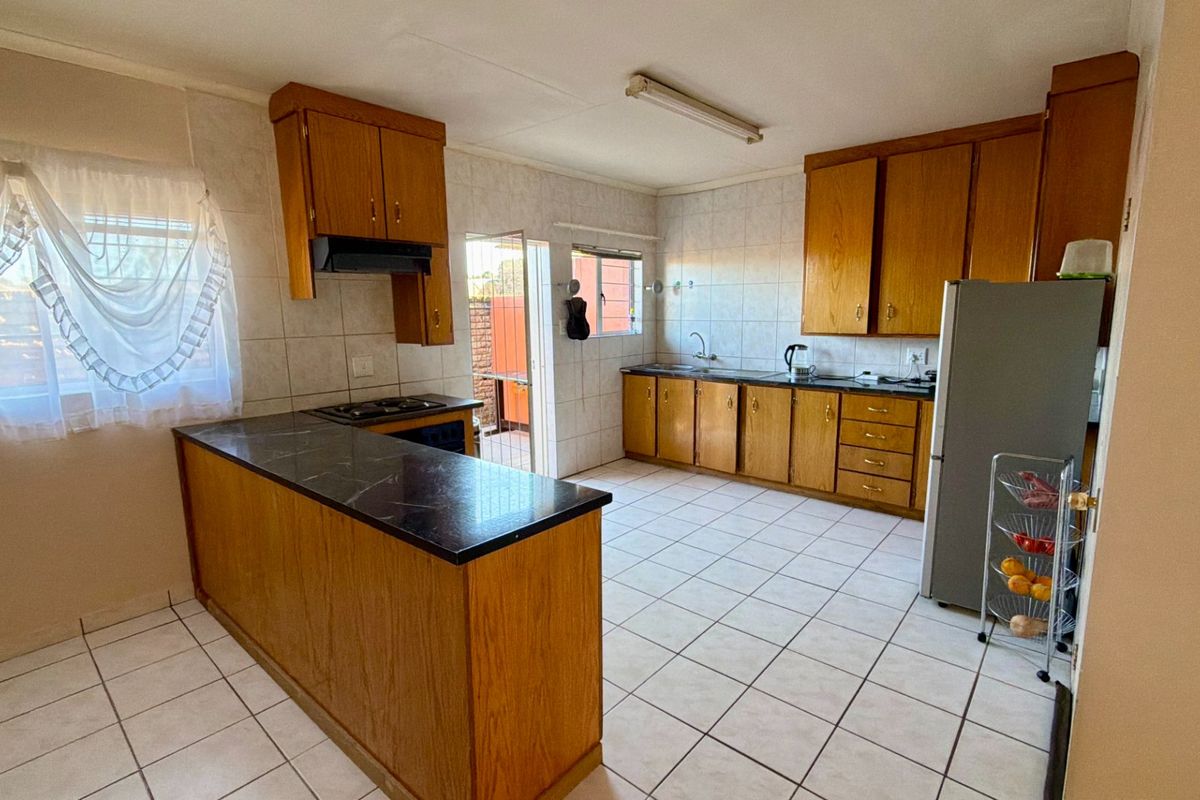 Functional kitchen featuring wooden cabinetry, laminate countertops, built-in hob with extractor fan, and tiled flooring with direct access to an outdoor area.