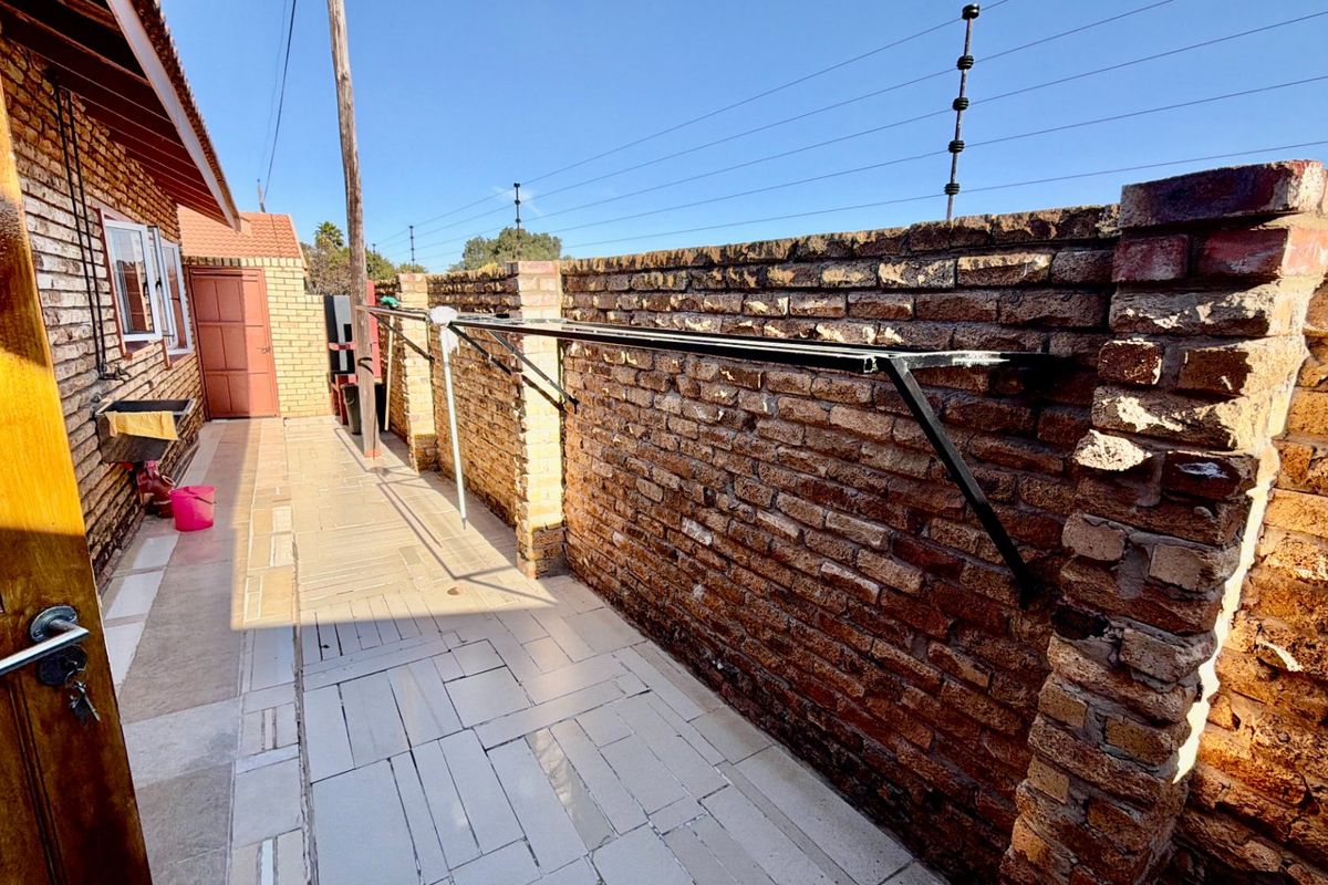 A paved rear exterior area featuring a brick boundary wall with electric fencing and a wall-mounted washing line.