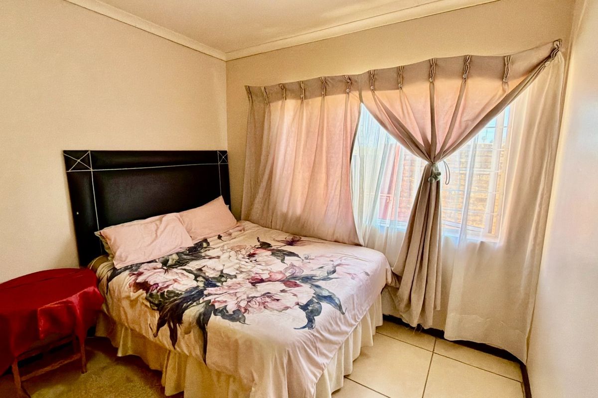 A functional bedroom featuring tiled flooring and a large window with installed curtain rails, providing natural light to the space.