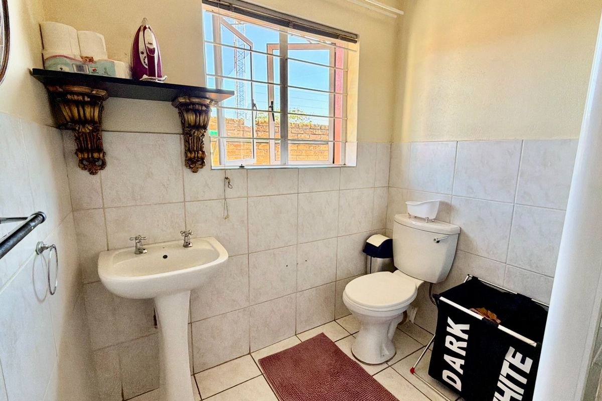 A functional bathroom featuring a pedestal basin, toilet, and tiled finishes with natural light from a window fitted with security bars.