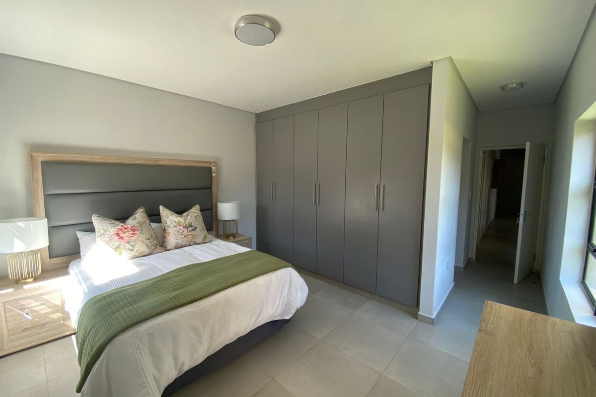 A well-maintained bedroom featuring neutral tiled flooring, modern grey built-in cupboards, and a clean, contemporary aesthetic.