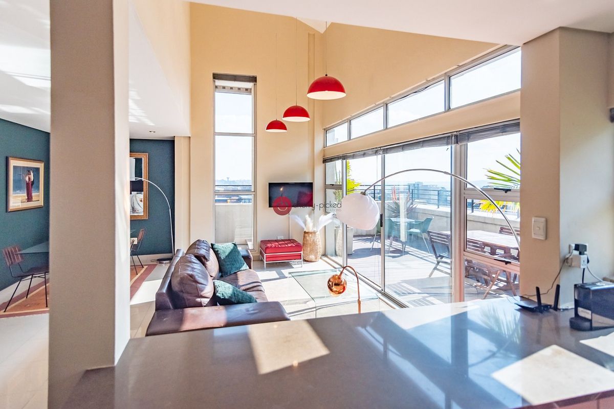 Spacious open-plan living area featuring high vaulted ceilings, large windows, and seamless access to an expansive outdoor balcony.
