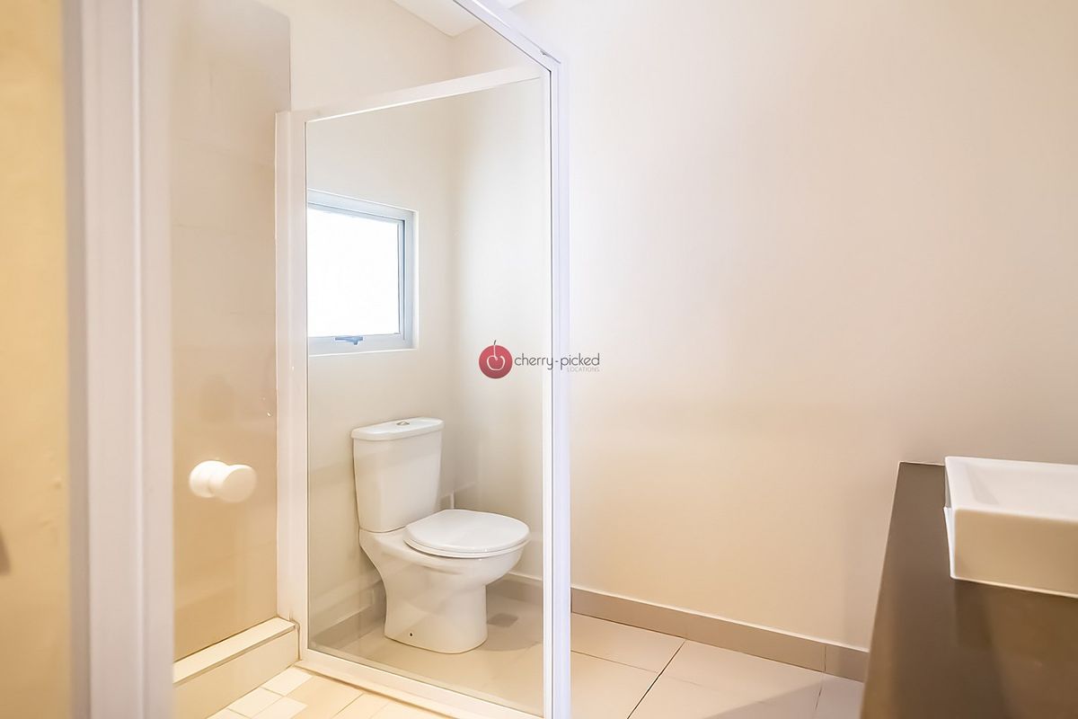 A clean and functional bathroom featuring a glass-enclosed shower, a modern toilet, and a vanity basin with neutral tiling.