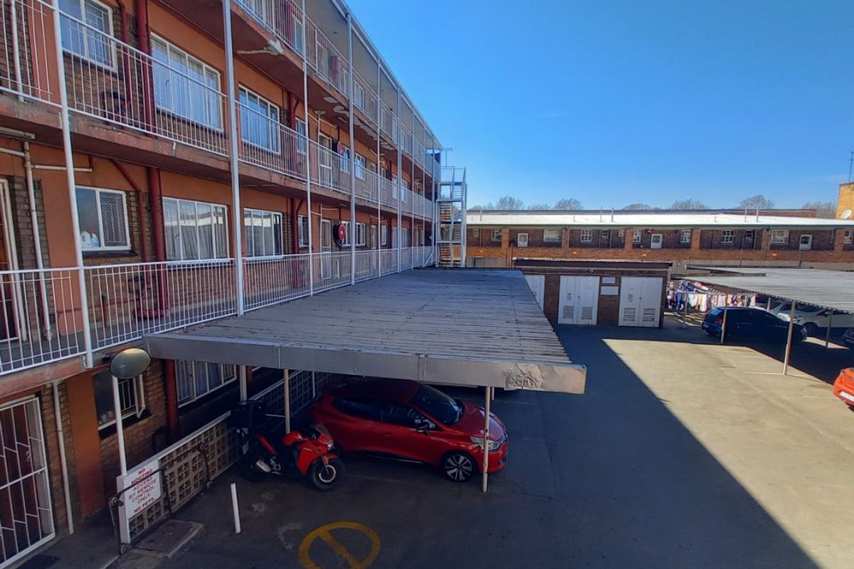 Exterior view of an apartment complex featuring covered parking bays and multi-level balconies with metal railings.