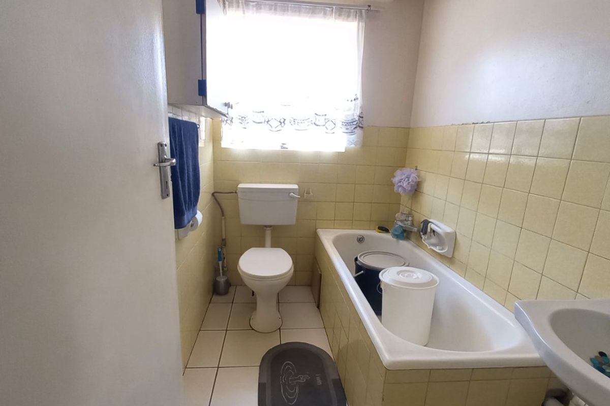 A compact bathroom featuring a bathtub, toilet, and pedestal basin with dated yellow wall tiling and neutral floor tiles.