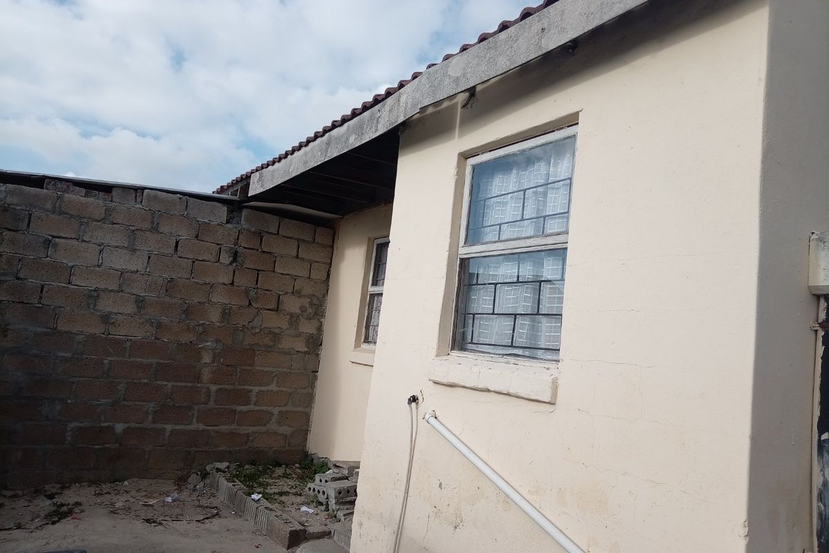 Rear exterior view of the property featuring a concrete block boundary wall, tiled roof, and windows with security bars.