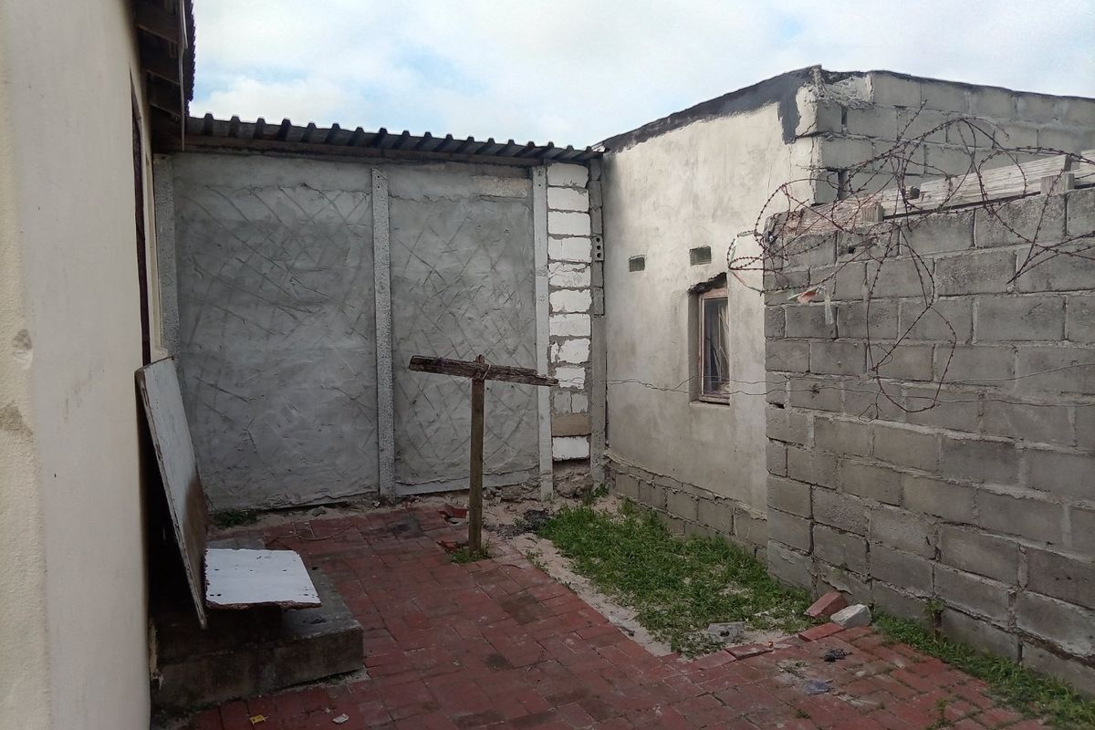 A rear exterior area featuring brick paving and concrete boundary walls with barbed wire fencing, showing signs of wear and unfinished construction.
