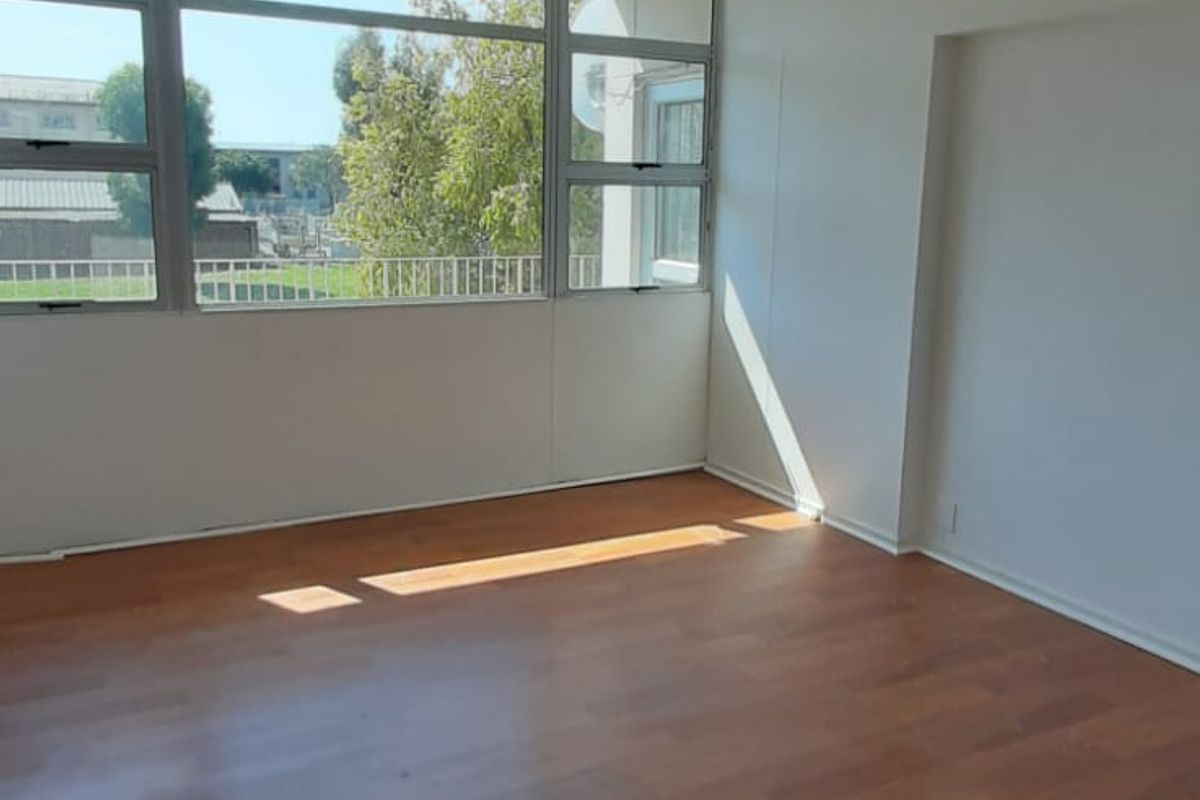 A bright, empty living room featuring laminate flooring and large windows that provide ample natural light and an exterior view.