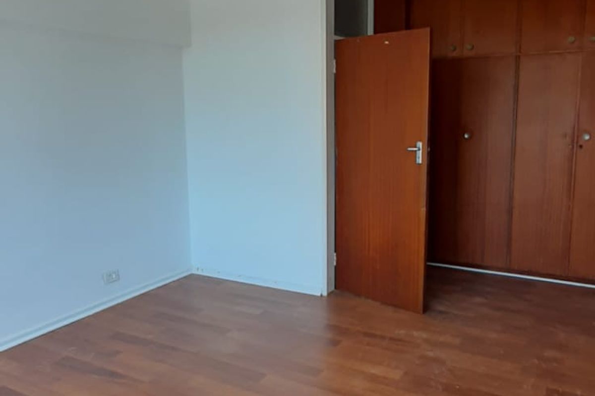 An empty bedroom featuring wooden flooring and built-in wooden cupboards, offering a blank canvas for potential interior design updates.