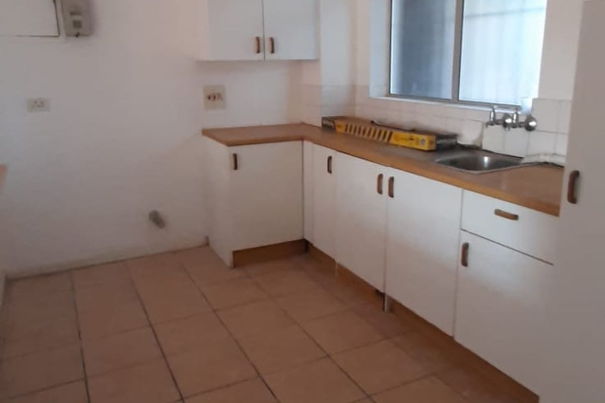 A functional, empty kitchen featuring white cabinetry, laminate countertops, a stainless steel sink, and tiled flooring, ready for modernization.