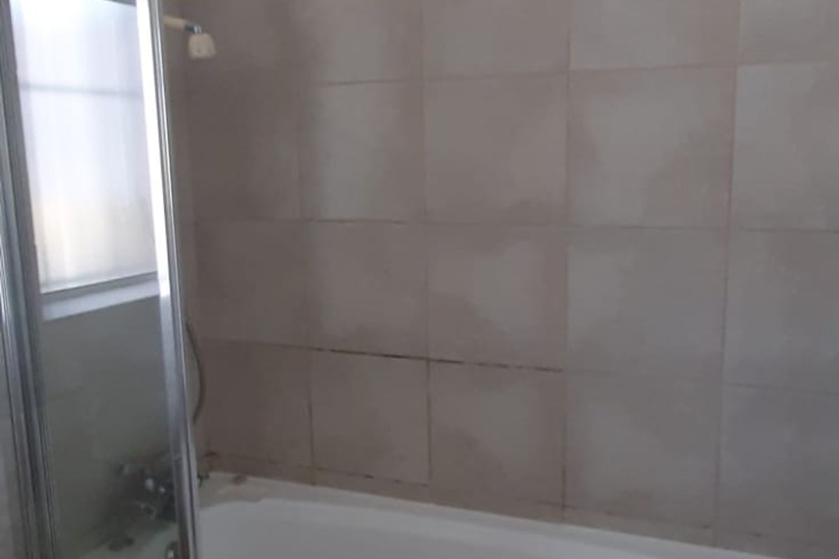 A functional bathroom featuring a bathtub with a glass shower screen, tiled walls and flooring, and a standard toilet.
