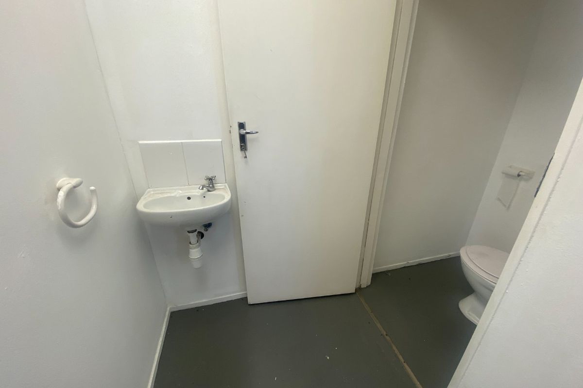 A functional industrial-style restroom featuring a wall-mounted basin and a separate toilet cubicle with basic finishes.