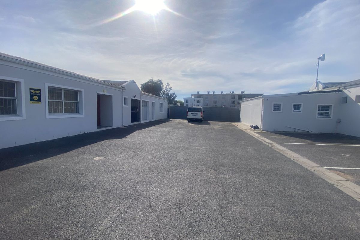 A paved industrial courtyard area providing access to multiple building units with security bars on windows and perimeter fencing.