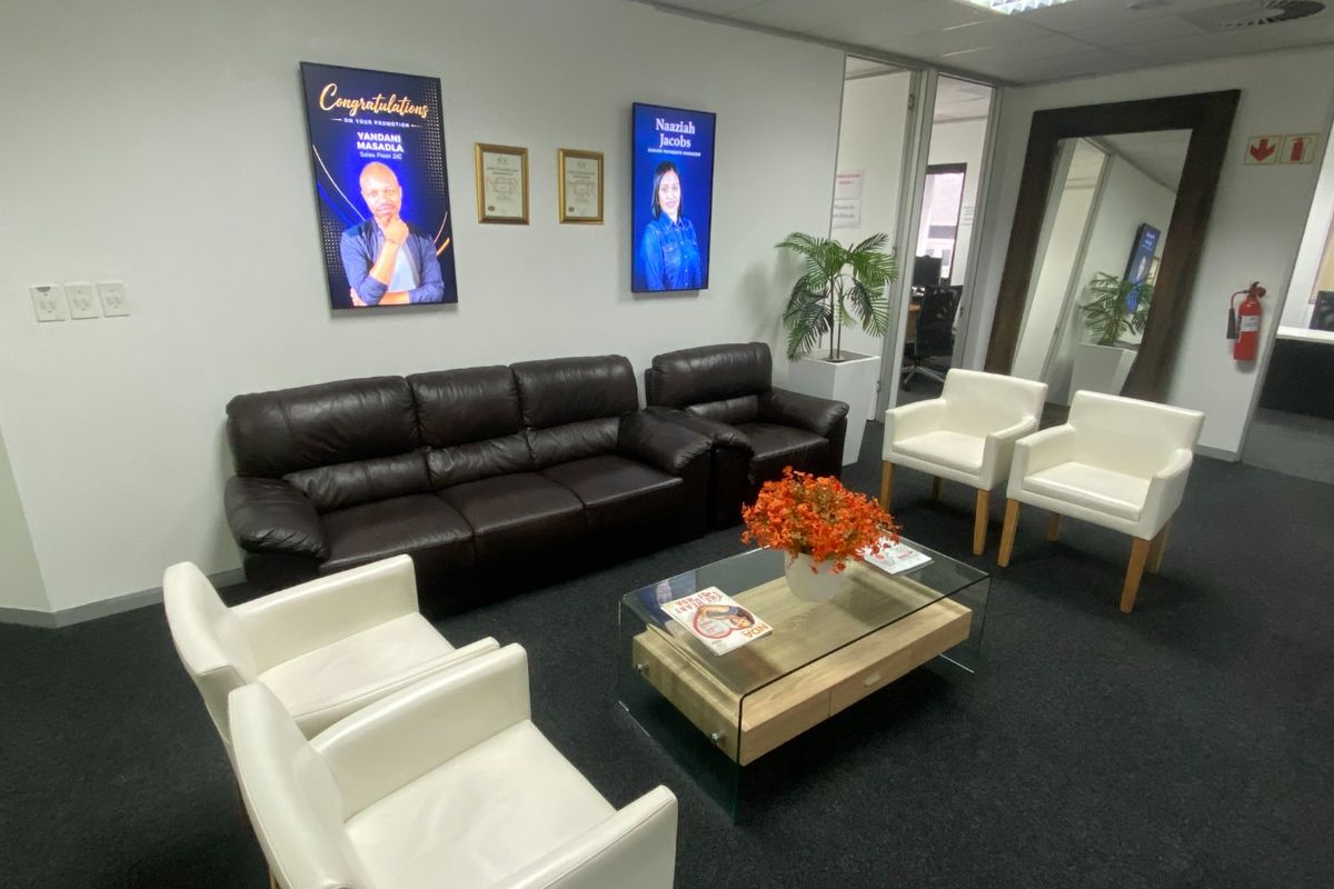 A professional commercial waiting area or lounge featuring dark carpeting, recessed ceiling lighting, and glass partition walls.