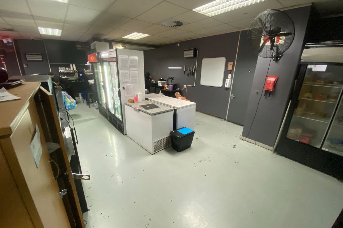 Commercial kitchen space featuring industrial flooring, suspended ceiling lighting, and wall-mounted ventilation, suitable for food preparation and storage operations.