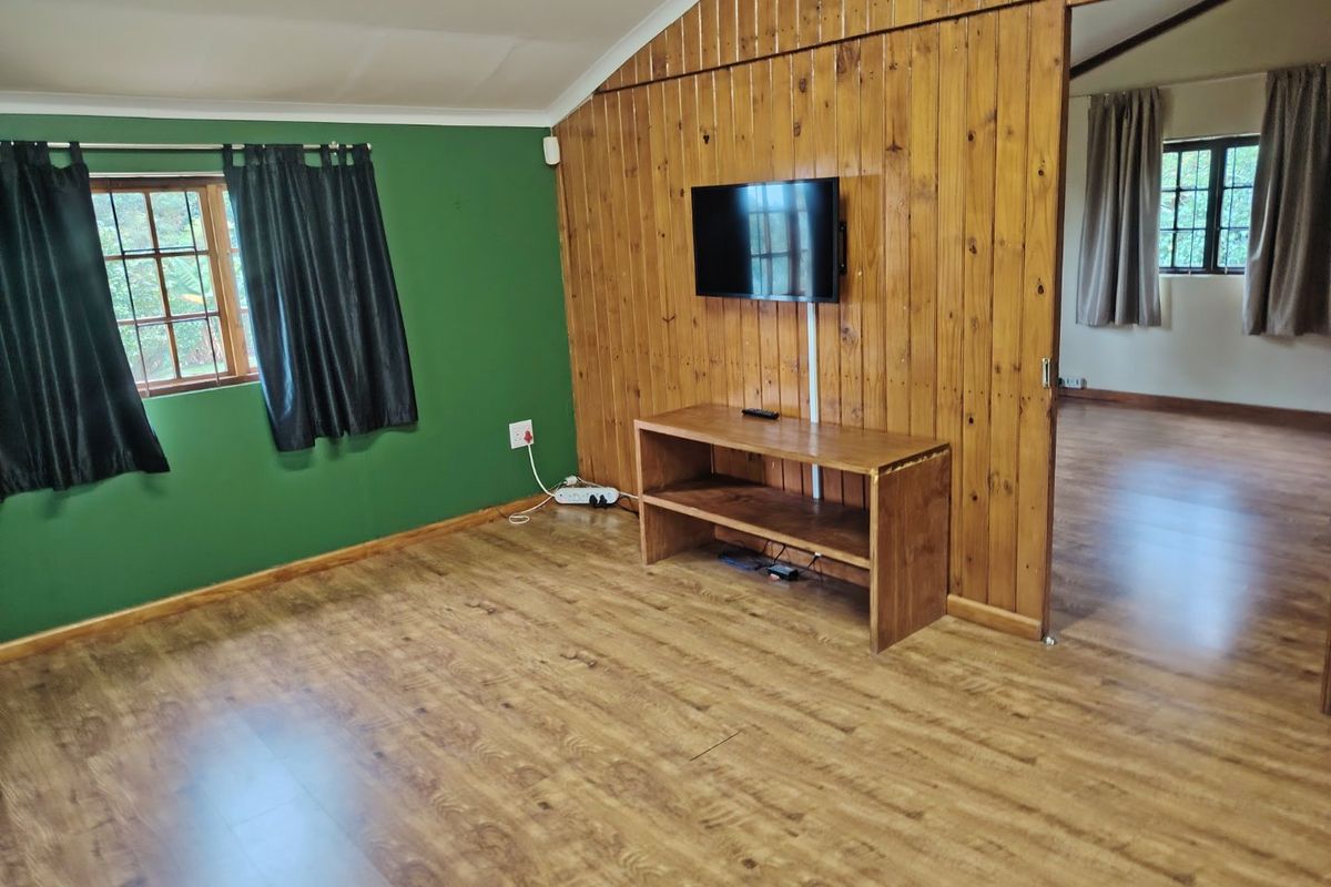 A living room featuring timber wall paneling, laminate flooring, and a sliding door leading to an adjacent room.