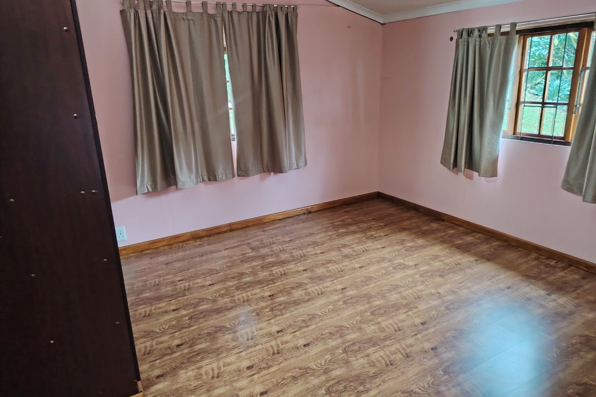 A vacant bedroom featuring laminate wood-look flooring, timber skirting boards, and timber-framed windows with neutral curtains.
