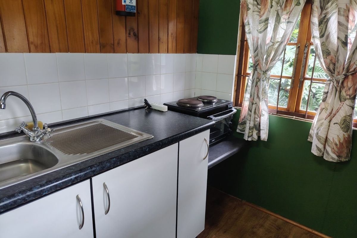 Compact kitchen featuring white cabinetry, dark laminate countertops, tiled splashback, and timber wall paneling with a functional sink and window view.
