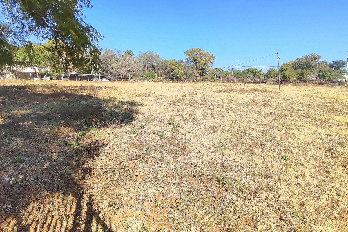 A vacant residential plot of land featuring dry grass, perimeter fencing, and utility poles, offering a clear space for future development.