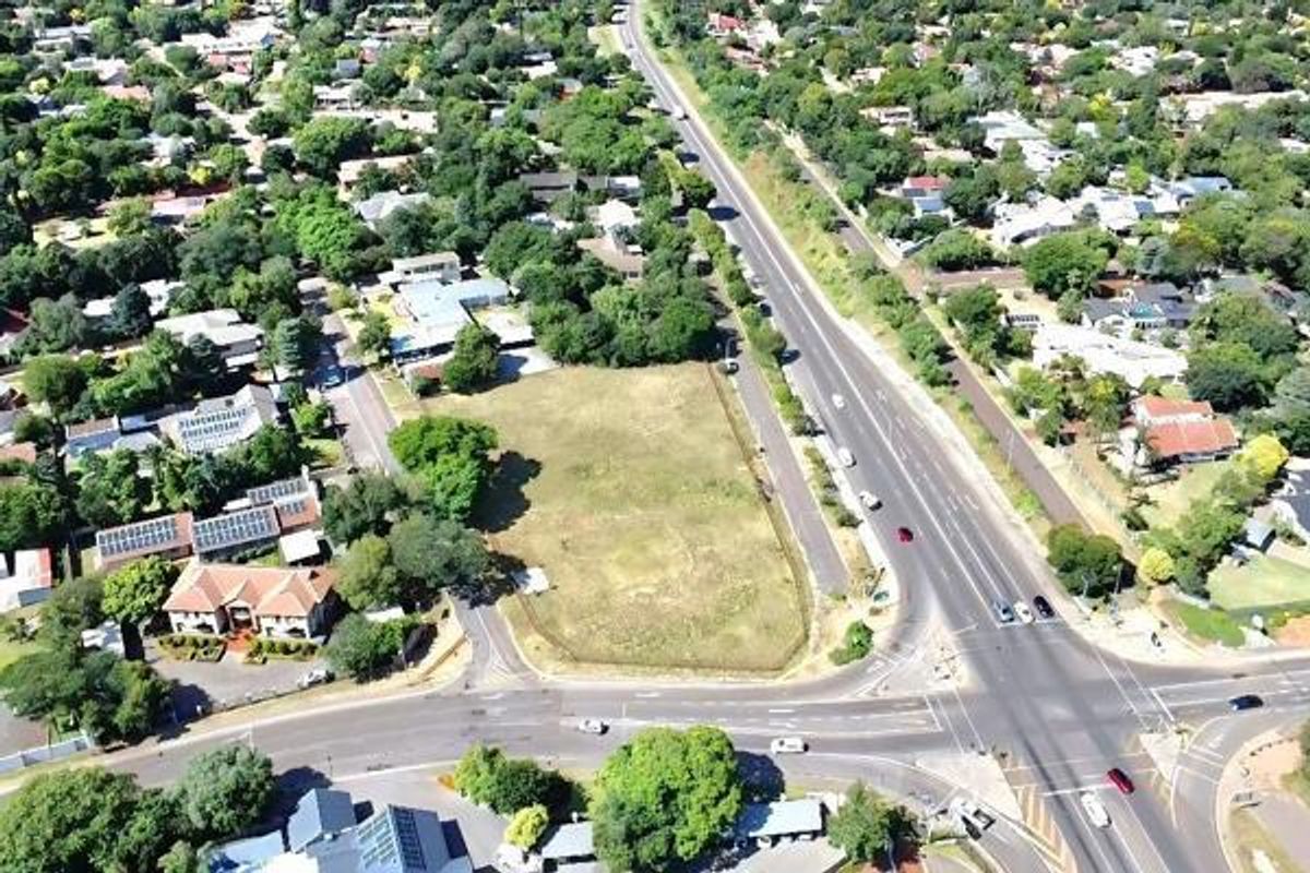 An aerial view of a vacant residential corner plot situated in a well-established suburban neighborhood with mature trees and road access.