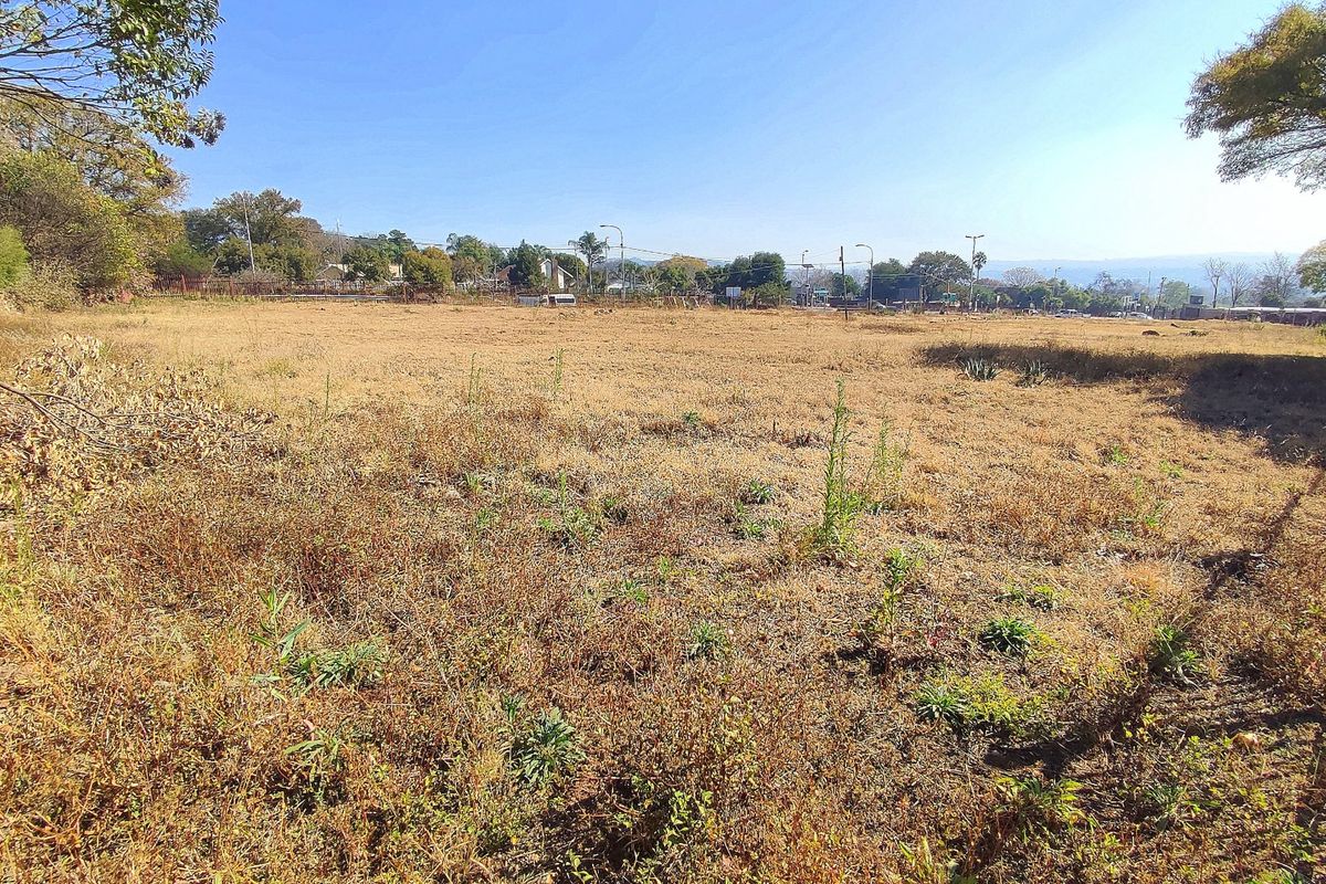 A wide-angle view of a vacant residential plot featuring dry grass and perimeter fencing, suitable for future development.