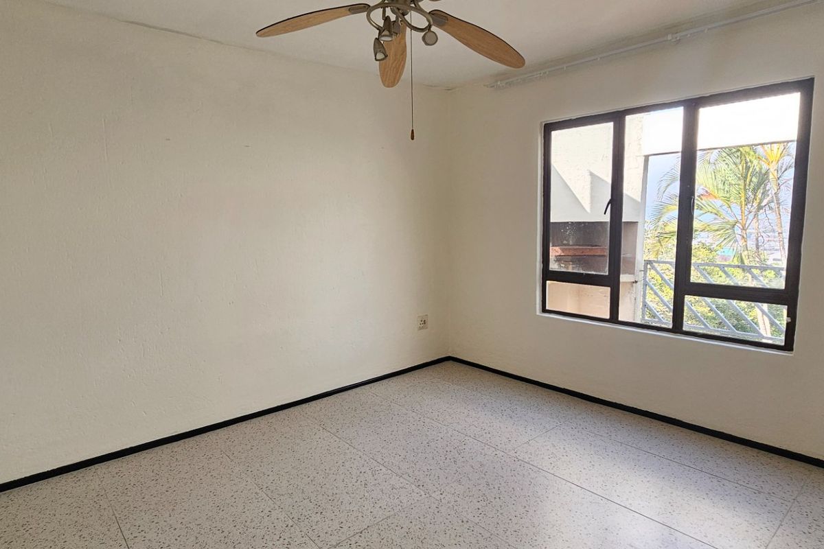 A bright, empty bedroom featuring terrazzo flooring, a ceiling fan, and large windows providing natural light.