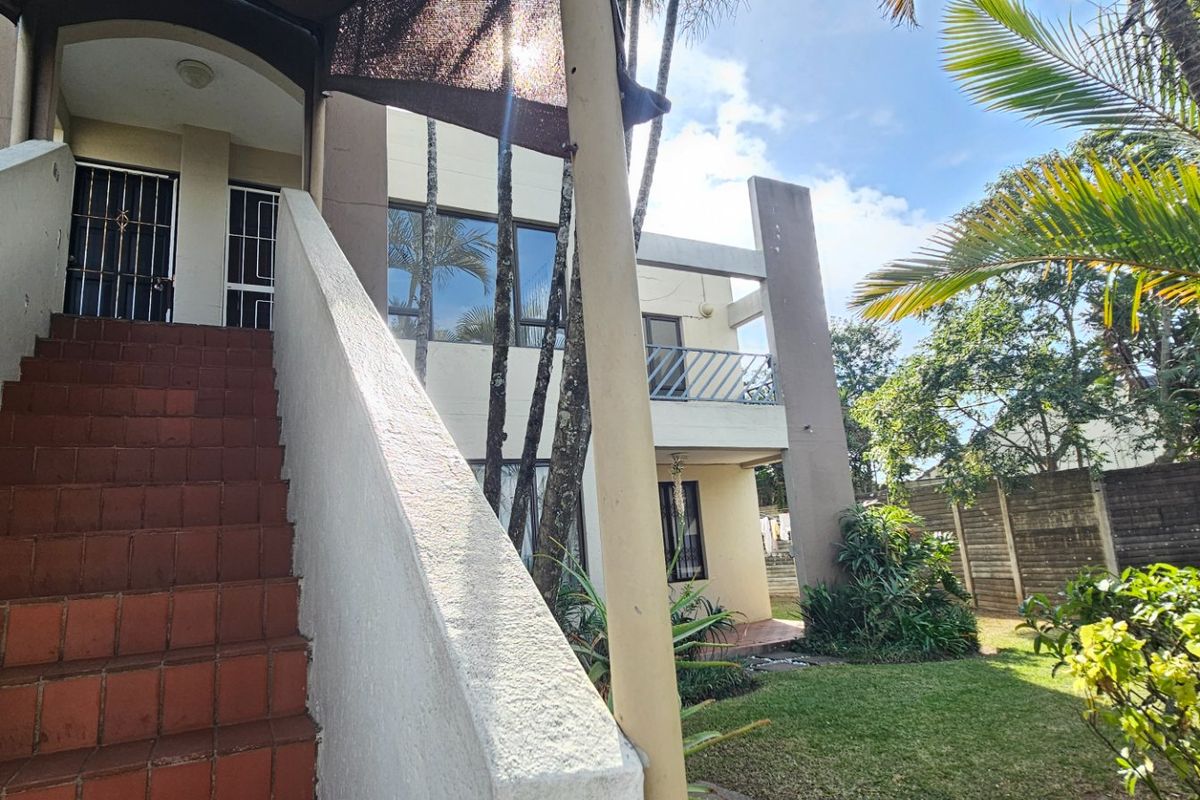 Exterior view of an apartment building featuring a tiled staircase leading to an upper level, a balcony, and a small garden area.